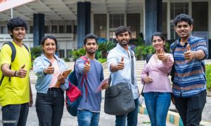 Confident students with backpack showing thumbs up by looking at camera at college campus - concept of approval, education and development